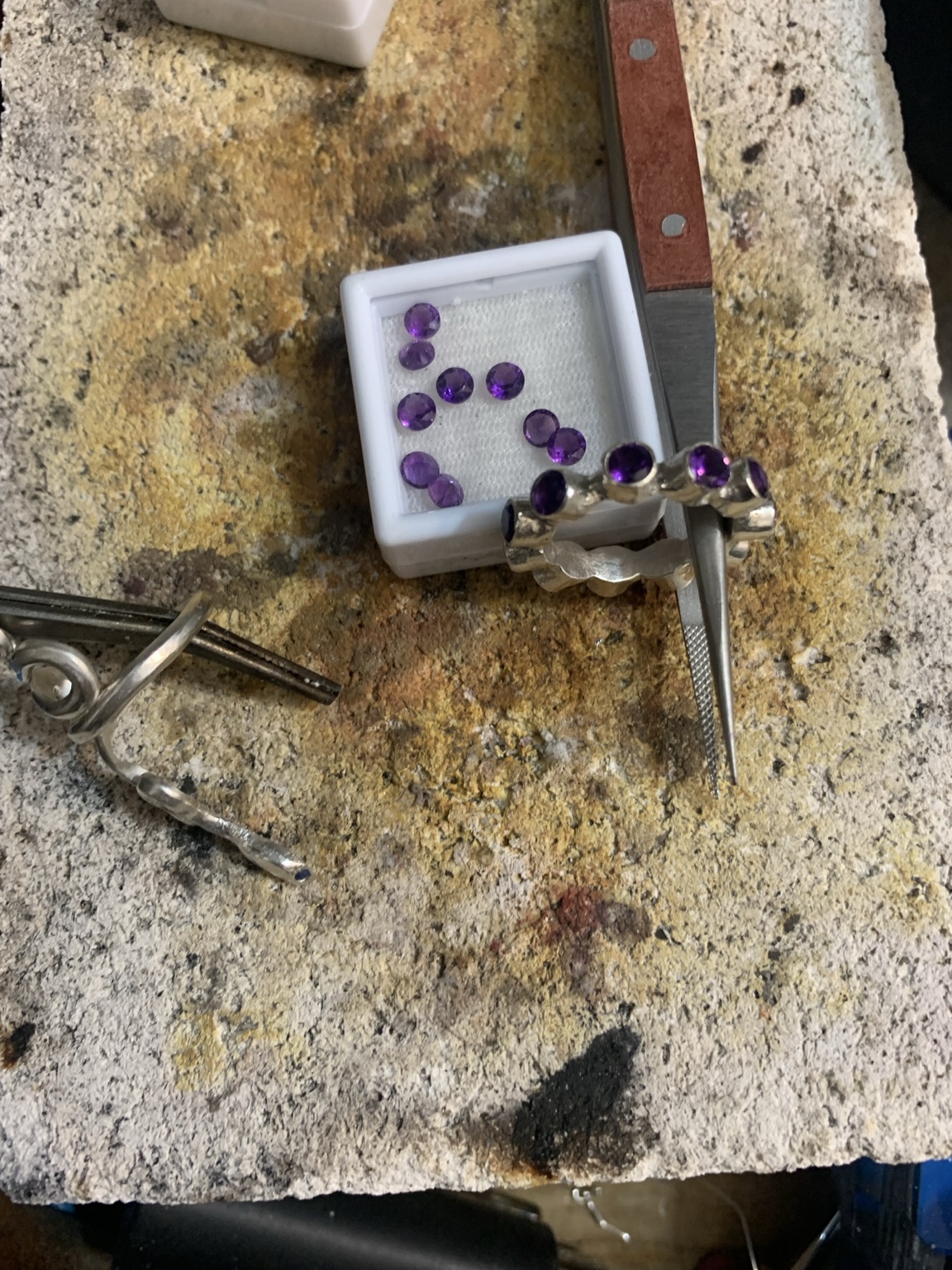 Purple stones and a partially set ring on a soldering block beside hand tools