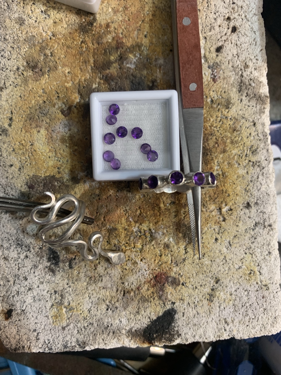Jewelry in progress with loose stones, wire, and tools on the workbench