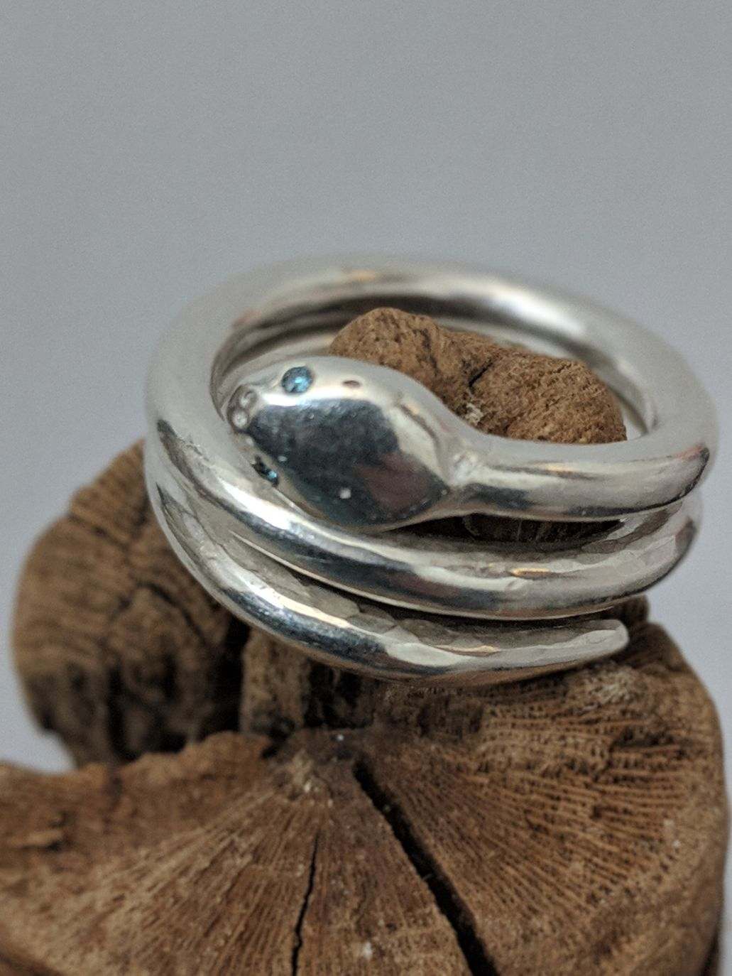 Coiled snake ring with blue eyes displayed on wood